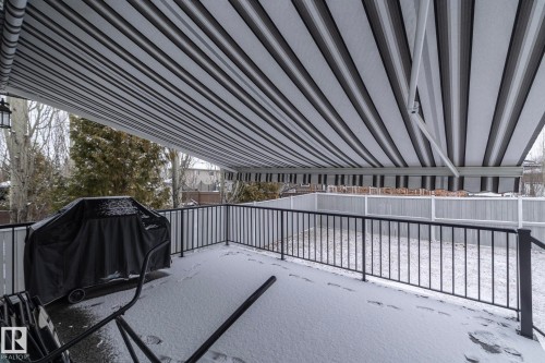 Outdoor deck space with a striped retractable awning, black metal railing, and privacy fencing - 307 Ravine Close, Devon, AB - Outdoor With Exterior