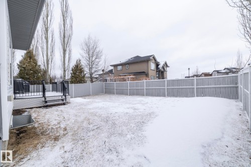 The property features a spacious yard with a deck, partially covered in snow, and enclosed by a light grey fence - 307 Ravine Close, Devon, AB - Outdoor