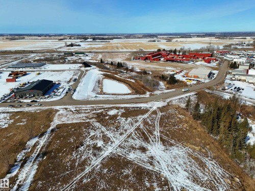 Aerial view of the property and its surrounding area, featuring cleared land, a paved road, and distant buildings - 307 Ravine Close, Devon, AB - Outdoor With View