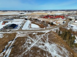 Aerial view of the property and its surrounding area, featuring cleared land, a paved road, and distant buildings - 