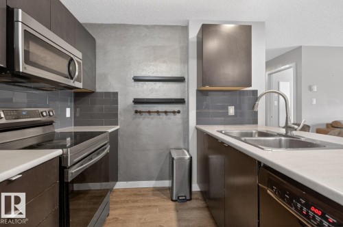 The kitchen features dark cabinetry, a stainless steel microwave, and a double basin sink with a gooseneck faucet - 109 340 Windermere Road, Edmonton, AB 