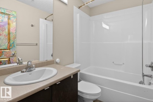 The bathroom features a vanity with a countertop and undermount sink, a toilet, and a bathtub with a shower - 109 340 Windermere Road, Edmonton, AB 