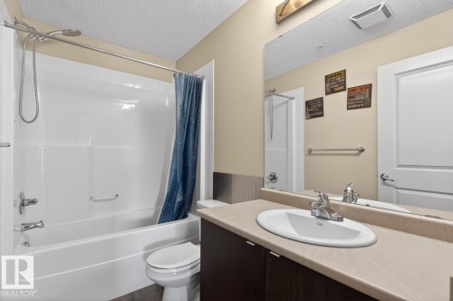 Bathroom featuring a white bathtub with a shower, a vanity with a light-colored countertop, and a large mirror - 109 340 Windermere Road, Edmonton, AB 