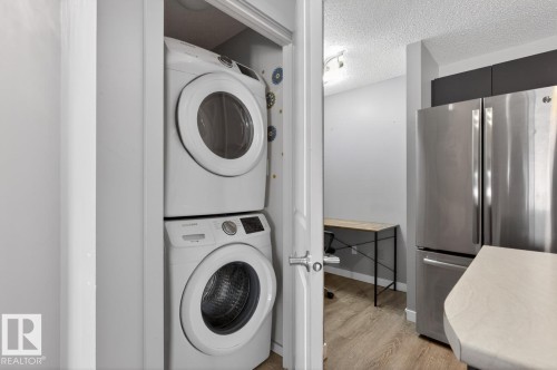 This property features a convenient stacked washer and dryer unit, a stainless steel refrigerator, and wood-look flooring - 109 340 Windermere Road, Edmonton, AB 