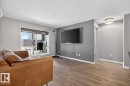 This living area features light wood-look flooring, light grey walls, and a sliding glass door providing access to a patio - 109 340 Windermere Road, Edmonton, AB 