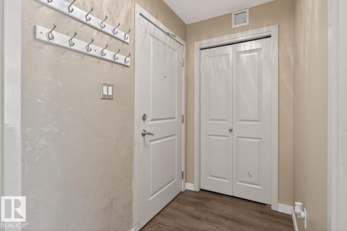 The property's entryway features a white door, light-colored walls, and two wall-mounted coat racks - 109 340 Windermere Road, Edmonton, AB 