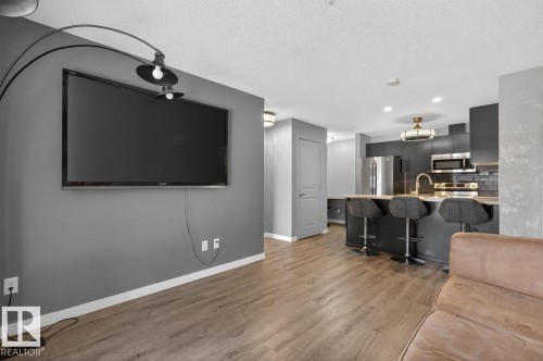 Living area featuring wide plank flooring and an open concept kitchen with stainless steel appliances, dark cabinetry, and a peninsula with seating - 109 340 Windermere Road, Edmonton, AB 