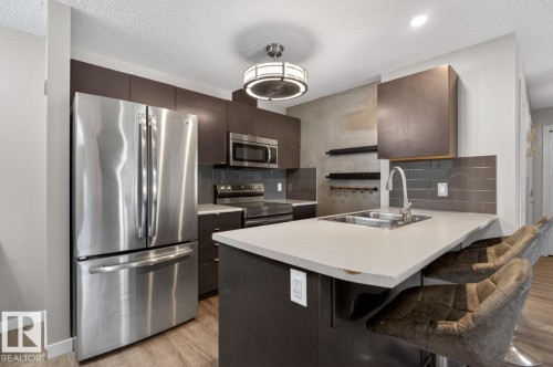 Well-appointed kitchen featuring stainless steel appliances, dark cabinetry, and a light-toned countertop with an integrated sink - 109 340 Windermere Road, Edmonton, AB 
