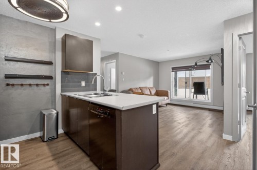 The property features an open concept kitchen and living area with wood-look flooring throughout - 109 340 Windermere Road, Edmonton, AB 