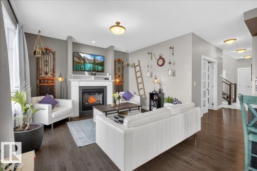 Inviting living area featuring rich hardwood floors, a fireplace with a white mantel, and ceiling light fixtures - 606 Reynalds Way, Leduc, AB - Indoor Photo Showing Living Room With Fireplace