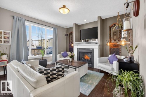 Living room featuring dark hardwood floors, a fireplace with a white mantel, and a large window providing natural light - 606 Reynalds Way, Leduc, AB - Indoor Photo Showing Living Room With Fireplace