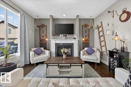 Living room featuring dark hardwood floors, a white fireplace with a dark insert, and a large window providing natural light - 606 Reynalds Way, Leduc, AB - Indoor Photo Showing Living Room With Fireplace