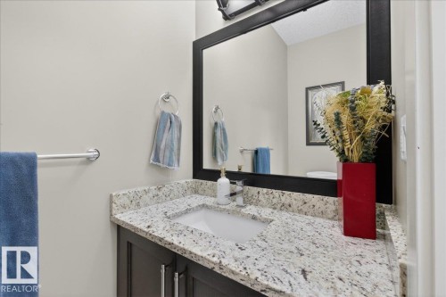 Bathroom vanity featuring a speckled countertop, an undermount sink, and a dark wood cabinet with chrome handles - 606 Reynalds Way, Leduc, AB - Indoor Photo Showing Bathroom