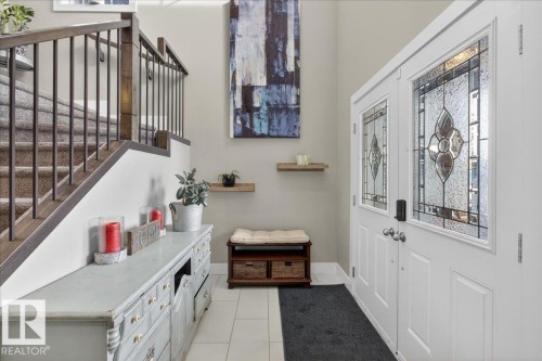 The property features a welcoming entryway with white double doors, each adorned with decorative glass panels - 606 Reynalds Way, Leduc, AB - Indoor Photo Showing Other Room