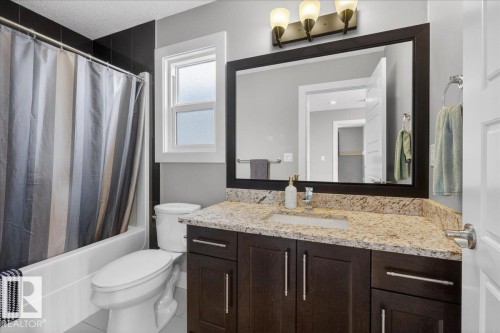 Bathroom featuring a vanity with granite countertop and dark wood cabinetry, a large framed mirror, and a full bathtub with a shower - 606 Reynalds Way, Leduc, AB - Indoor Photo Showing Bathroom