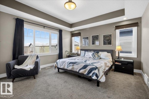Spacious bedroom featuring a tray ceiling, carpeted flooring, and large windows with dark curtains - 606 Reynalds Way, Leduc, AB - Indoor Photo Showing Bedroom