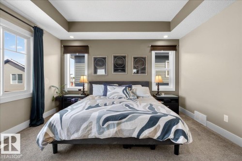 This bedroom features tray ceilings with recessed lighting, large windows, and a neutral color palette - 606 Reynalds Way, Leduc, AB - Indoor Photo Showing Bedroom
