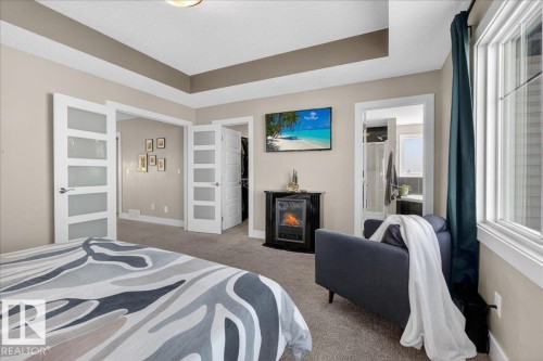 This bedroom features a tray ceiling, soft carpet flooring, and a large window with privacy blinds - 606 Reynalds Way, Leduc, AB - Indoor Photo Showing Bedroom