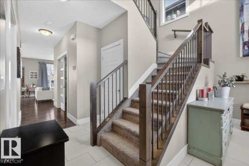 Entryway featuring light-colored floor tiles and a carpeted staircase with dark wood and metal railings - 606 Reynalds Way, Leduc, AB - Indoor Photo Showing Other Room