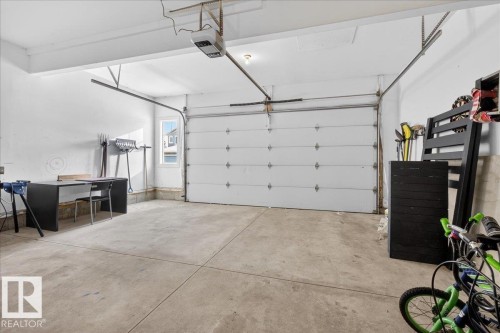 The property includes a spacious garage with a white sectional door, concrete flooring, and a single window providing natural light - 606 Reynalds Way, Leduc, AB - Indoor Photo Showing Garage