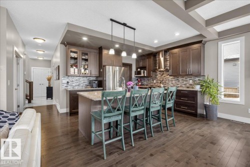Open concept living space featuring hardwood floors, a kitchen island with seating, dark wood cabinetry, and stainless steel appliances - 606 Reynalds Way, Leduc, AB - Indoor Photo Showing Kitchen With Upgraded Kitchen