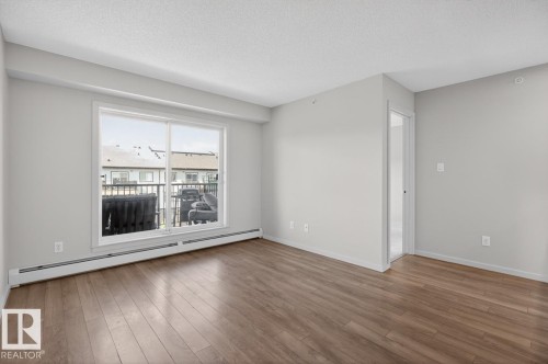 This room features light-colored walls, hardwood flooring, and a sliding glass door leading to an outdoor space - 426 390 Windermere Road, Edmonton, AB - Indoor