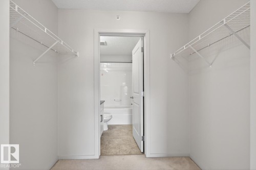 This property features a closet with white wire shelving, leading to a bathroom with a white tub and toilet, and a vanity with a gray countertop - 426 390 Windermere Road, Edmonton, AB - Indoor Photo Showing Other Room