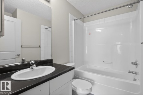 Bathroom featuring a vanity with a white oval sink, dark countertop, and a built-in tub with a shower - 426 390 Windermere Road, Edmonton, AB - Indoor Photo Showing Bathroom