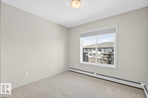 This room features light-colored walls and carpeting, a window with a roller shade, and baseboard heating - 426 390 Windermere Road, Edmonton, AB - Indoor Photo Showing Other Room