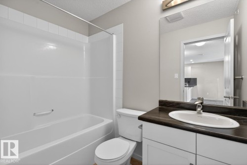 The bathroom features a white bathtub with a shower, a toilet, and a vanity with a dark countertop and an undermount sink - 426 390 Windermere Road, Edmonton, AB - Indoor Photo Showing Bathroom