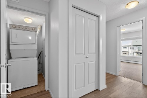 The property features a dedicated laundry area with a stacked washer and dryer, complemented by a hallway with wood-look flooring and a closet with bifold doors - 426 390 Windermere Road, Edmonton, AB - Indoor Photo Showing Laundry Room