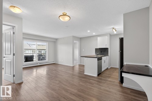 Open concept living space featuring wood flooring, a kitchen island, and a sliding glass door leading to a balcony - 426 390 Windermere Road, Edmonton, AB - Indoor