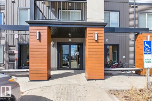 The property's entrance features dark double doors, a protective overhang, and a modern exterior with wood-paneled accents and wall-mounted lighting fixtures - 426 390 Windermere Road, Edmonton, AB - Outdoor With Balcony