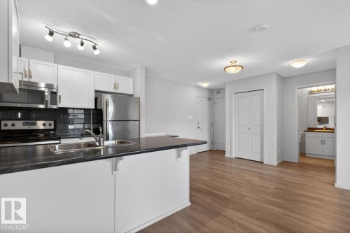 The property features a kitchen with white cabinetry, stainless steel appliances, and a dark countertop with an integrated sink - 426 390 Windermere Road, Edmonton, AB - Indoor Photo Showing Kitchen With Double Sink