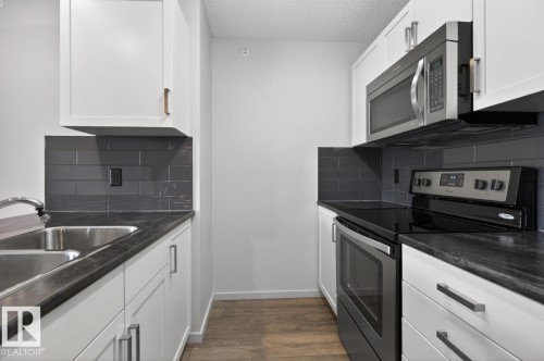 The kitchen features white cabinetry, dark countertops, and a dark subway tile backsplash - 426 390 Windermere Road, Edmonton, AB - Indoor Photo Showing Kitchen With Double Sink