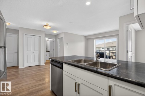 The kitchen features a double stainless steel sink and a stainless steel dishwasher, integrated into cabinetry with a dark countertop - 426 390 Windermere Road, Edmonton, AB - Indoor Photo Showing Kitchen With Double Sink