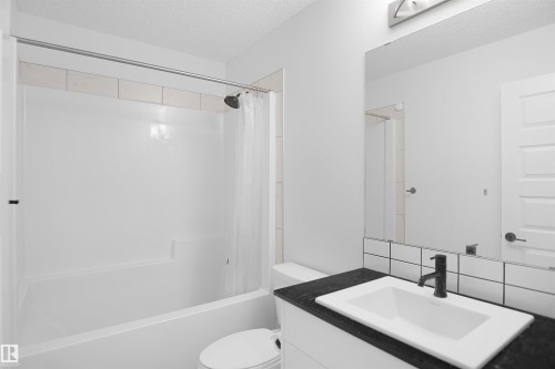 Bathroom featuring a white bathtub with a shower head, a white vanity with a dark countertop and a rectangular sink, and a large wall-mounted mirror - Edmonton, AB - Indoor Photo Showing Bathroom