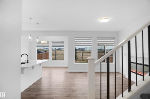 Open concept living area featuring hardwood flooring, a white kitchen island with a dark faucet, and large windows with blinds - Edmonton, AB - Indoor Photo Showing Other Room