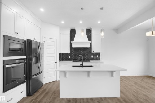Modern kitchen featuring white cabinetry, a large kitchen island with a sink, stainless steel appliances, and a dark subway tile backsplash - Edmonton, AB - Indoor Photo Showing Kitchen With Upgraded Kitchen