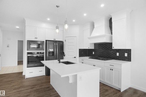The kitchen features white cabinetry, a large island with a sink, a black subway tile backsplash, and dark stainless steel appliances - Edmonton, AB - Indoor Photo Showing Kitchen With Upgraded Kitchen