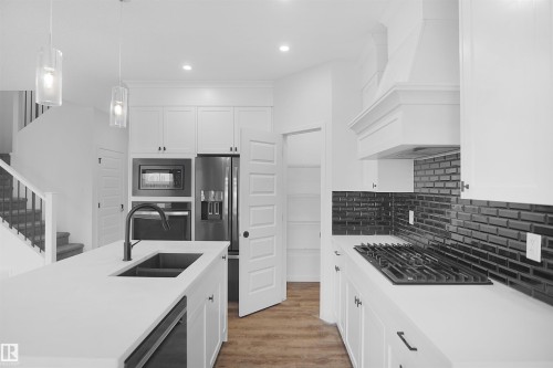 The kitchen features white cabinetry, a dark subway tile backsplash, and a large island with an integrated sink - Edmonton, AB - Indoor Photo Showing Kitchen With Double Sink With Upgraded Kitchen