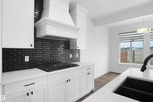 The kitchen features white cabinetry, a dark subway tile backsplash, a built-in range, and a large window providing views of the open landscape - Edmonton, AB - Indoor Photo Showing Kitchen With Upgraded Kitchen