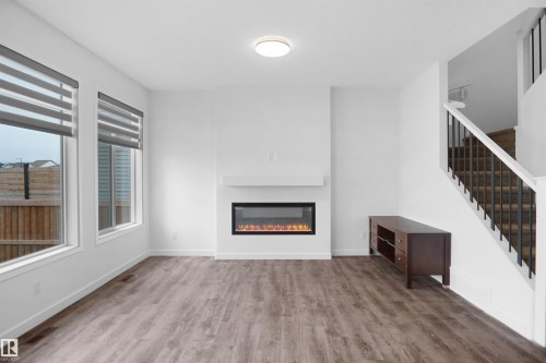 Bright living area featuring wide plank flooring, an electric fireplace with a white mantel, and two large windows with blinds - Edmonton, AB - Indoor Photo Showing Other Room With Fireplace