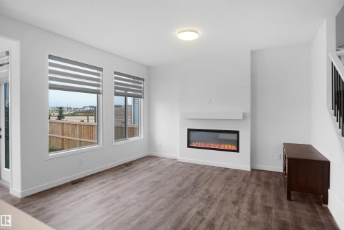 Living area featuring two large windows with blinds, an electric fireplace with a white mantel, and wood-style flooring - Edmonton, AB - Indoor Photo Showing Living Room With Fireplace