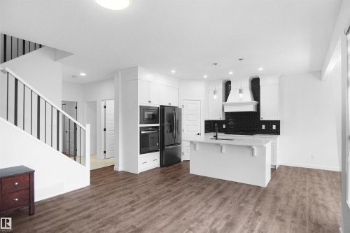 Open concept living area featuring dark wood-style flooring, a white kitchen island with a dark faucet, white kitchen cabinetry, and black appliances - Edmonton, AB - Indoor Photo Showing Kitchen