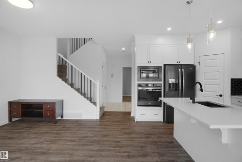 Open concept living area featuring dark wood-style flooring and a staircase with white risers and handrails - Edmonton, AB - Indoor Photo Showing Kitchen With Upgraded Kitchen
