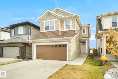 The property features a two-story design with light-colored siding, a brown garage door, and a concrete driveway - Edmonton, AB - Outdoor With Facade