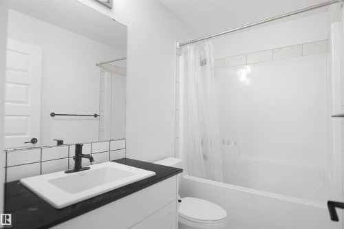 Bathroom featuring a vanity with a dark countertop and white sink, a mirror, and a bathtub with a shower - Edmonton, AB - Indoor Photo Showing Bathroom