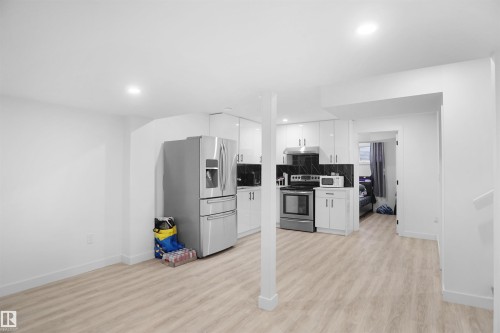 The property features a bright kitchen area with white cabinetry, stainless steel appliances, and a dark tile backsplash - Edmonton, AB - Indoor Photo Showing Kitchen