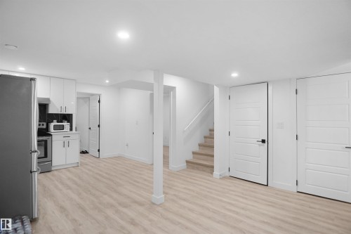 This property features a bright and spacious open area with light wood-style flooring, a functional kitchen with white cabinetry and a black tiled backsplash, and stairs with a light-colored handrail - Edmonton, AB - Indoor